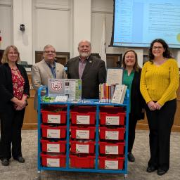 3 Library staff and 2 City leaders pose behind Community Comfort Cart at city council meeting. 