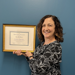 Milavec smiling and holding a framed award of appreciation from the Illinois Library Association.