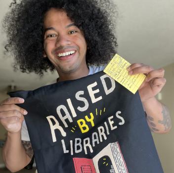 Mychal Threets holds up a T-shirt that says "Raised by Libraries"
