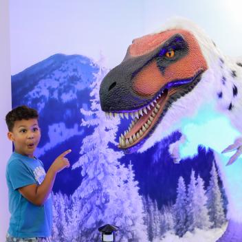 Small boy pointing at large white dinosaur. 