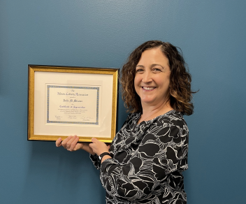 Milavec smiling and holding a framed award of appreciation from the Illinois Library Association.